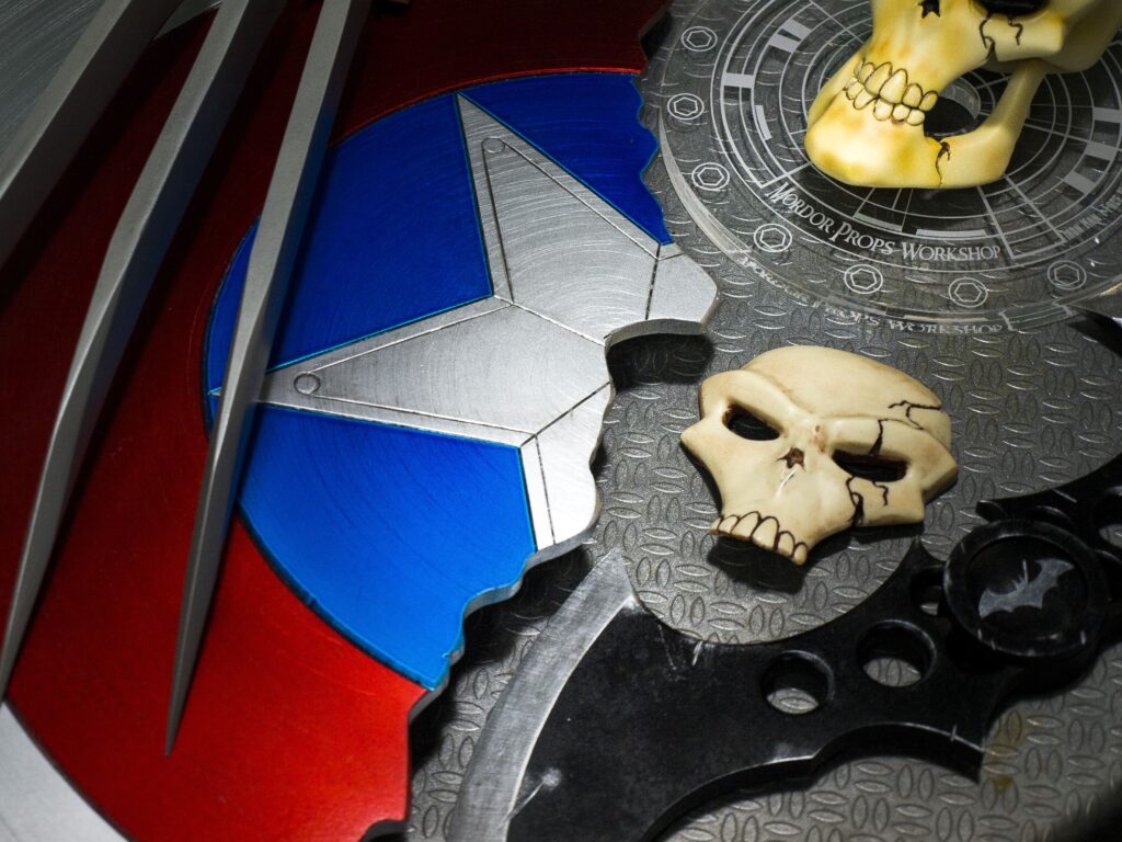 Escudo del Capitán América junto a garras de Lobezno, batarang y cráneos decorativos.